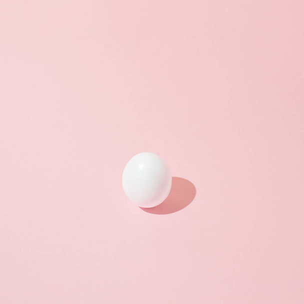 Huevo de Pascua blanco sobre fondo rosa con sombra aguda. Concepto mínimo. - Foto, imagen