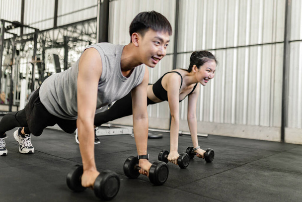 exercise concept The female and male members of the gym doing the basic renegade row posture with dumbbells while looing at each other face. - Photo, Image