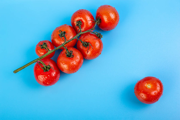 На синьому тлі лежала купка свіжих червоних помідорів з зеленими стеблами. Концепція рецепту, італієвої їжі, інгредієнту, соку, харчування, вітамінів. - Фото, зображення
