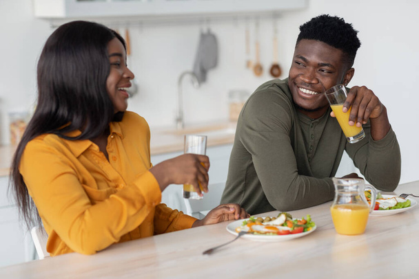 Χαρούμενο νεαρό μαύρο ζευγάρι κάθεται στο τραπέζι και τρώει νόστιμο πρωινό μαζί - Φωτογραφία, εικόνα