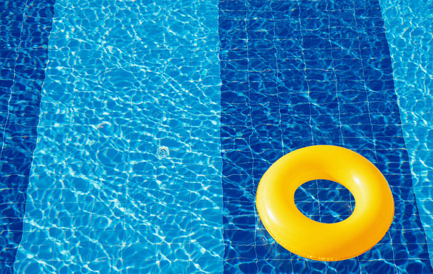 Geel zwembad drijvend, ring drijvend in een verfrissend blauw zwembad - Foto, afbeelding