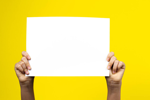 Kezek tartó üres fehér papírlap poszter plakát sárga alapon - Fotó, kép