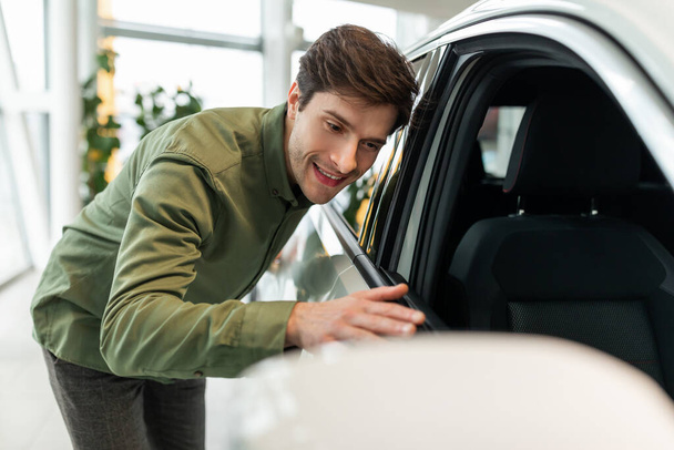 Happy young guy touching his new car, excited about buying automobile at dealership centre, copy space - Foto, Imagem