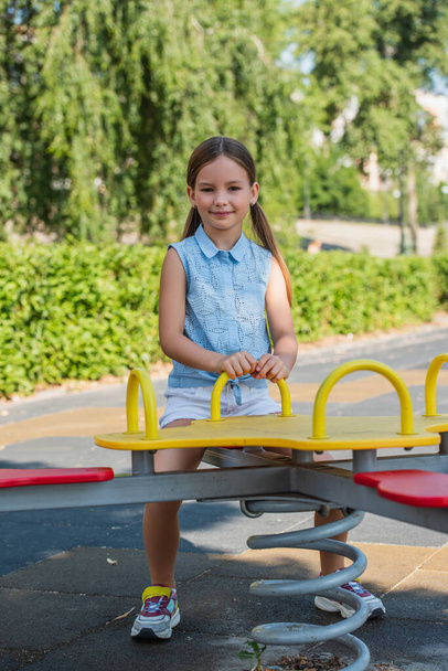 happy girl looking at camera while riding seesaw in park - Photo, Image