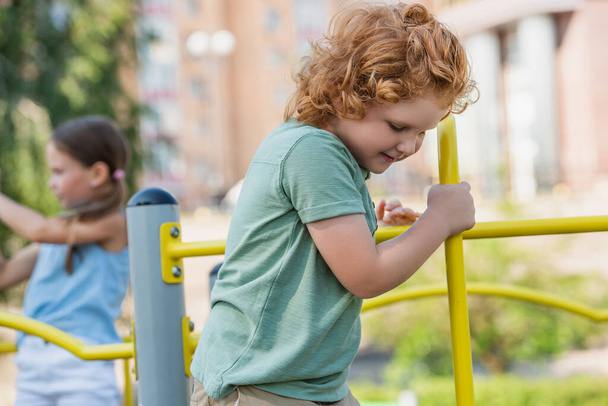 chico rizado jugando cerca borrosa chica en el patio de recreo - Foto, imagen