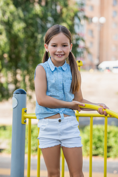 joyful girl in sleeveless blouse and short smiling at camera on playground - Fotoğraf, Görsel