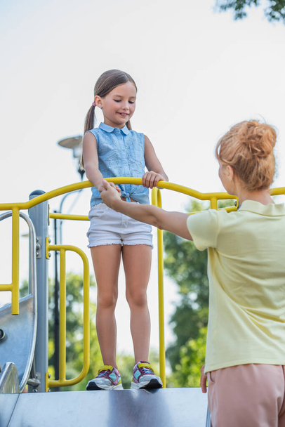 woman holding hand of daughter standing on slide in amusement park - Foto, immagini