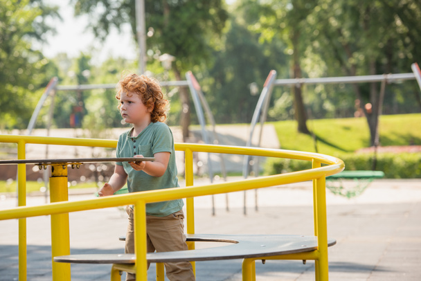 kudrnatý chlapec baví na kolotoči v letním parku - Fotografie, Obrázek