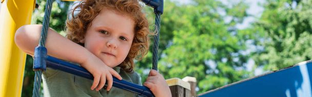 boy looking at camera from rope ladder in amusement park, banner - Photo, Image