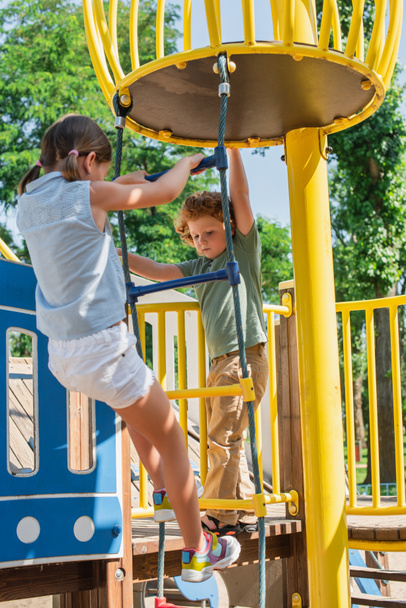 irmão e irmã subindo na escada de corda enquanto se divertindo no parque de diversões - Foto, Imagem