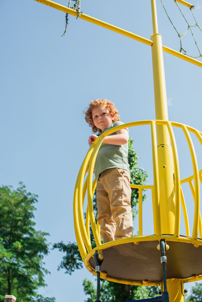 low angle view of boy looking at camera from high tower in amusement park - Foto, Imagen