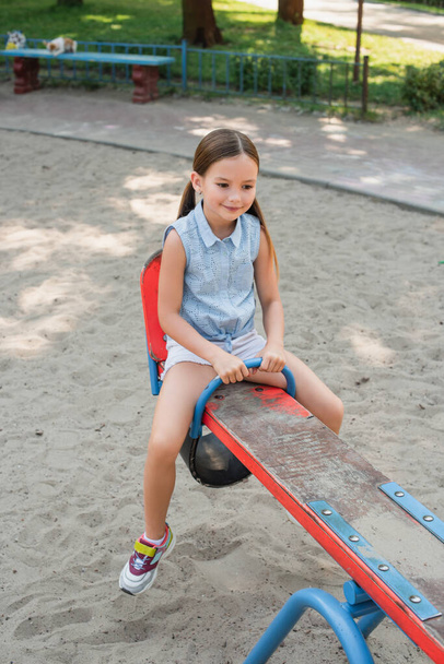 sonriente chica en pantalones cortos montar balancín en el parque de verano - Foto, Imagen