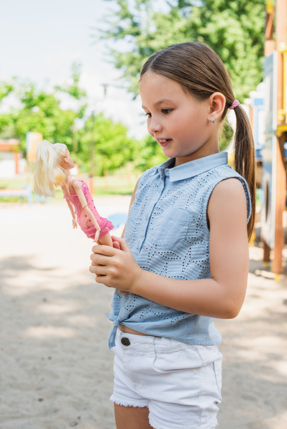 smiling girl in summer clothes holding doll outdoors - Photo, Image