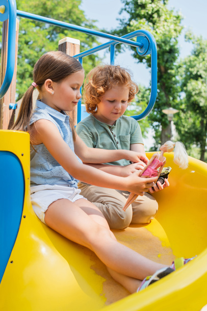 kinderen spelen met pop en speelgoed auto terwijl zitten op glijbaan - Foto, afbeelding