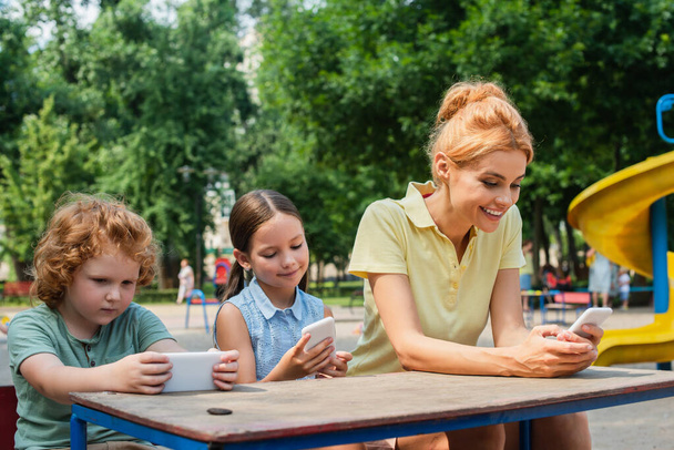 cheerful family using smartphones on playground in park - Foto, Imagem
