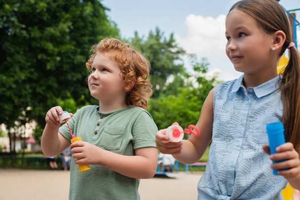 niños sosteniendo sopladores de burbujas mientras pasan tiempo al aire libre - Foto, imagen