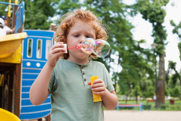 curly kid blowing soap bubbles on playground - Photo, Image