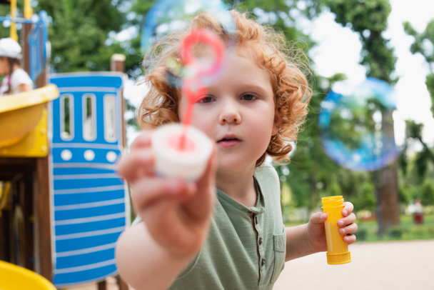 redhead boy looking at camera and showing blurred bubble blower - Photo, Image