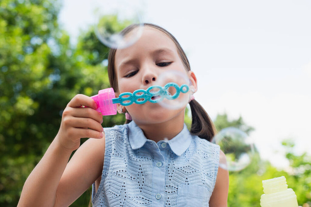 girl blowing soap bubbles on blurred foreground - Foto, Imagem