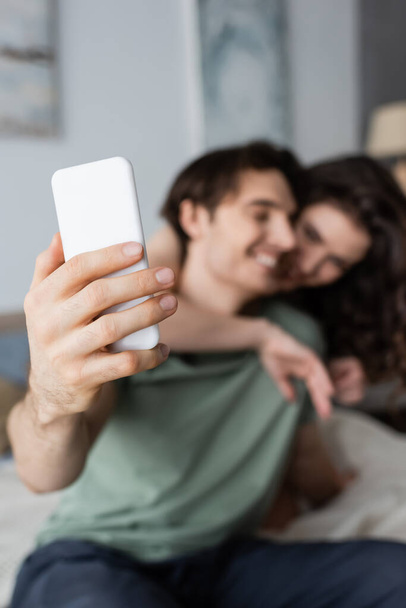 blurred happy couple taking selfie in bedroom - Foto, afbeelding