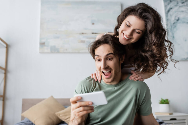 amazed man and woman looking at smartphone at home - Foto, imagen