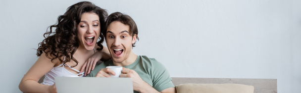 excited young couple looking at laptop in bedroom, banner - Photo, image