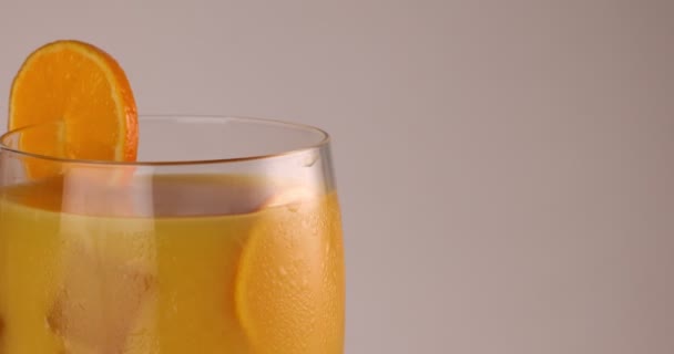close-up draaiend glas vullen met sinaasappelsap ijsblokje vorst op het glazen schijfje sinaasappel op de rand - Video