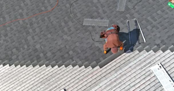 Eine Asphaltschindelanlage auf dem Dachdecker nagelt Asphaltschindeln an die Dachkonstruktion - Filmmaterial, Video