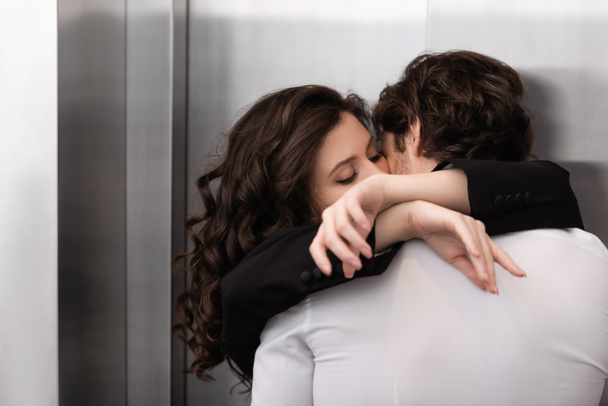 kręcone kobieta z zamkniętymi oczami całuje mężczyzna w pobliżu windy  - Zdjęcie, obraz