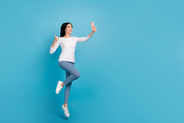 Full length body size view of beautiful trendy cheery girl jumping take selfie showing thumbup isolated on bright blue color background - Foto, Imagem