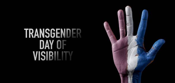 Поднятая рука человека, с нарисованным на ней флагом гордости трансгендера, и текстовый трансгендерный день видимости на черном фоне, в панорамном формате для использования в качестве веб-баннера или заголовка - Фото, изображение