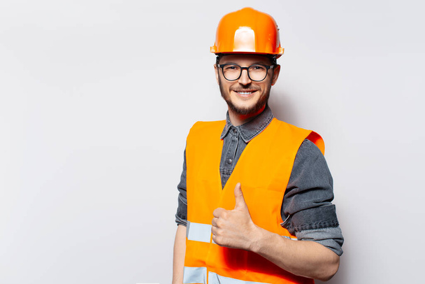 Photo d'un jeune constructeur de bâtiments. Portant un casque orange, le pouce levé. - Photo, image