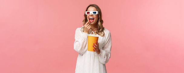 Tempo libero, uscire e concetto di primavera. Ritratto di giovane donna attraente in abito bianco godendo guardando film interessante a schermo intero al cinema, mangiare popcorn e indossare occhiali 3d
 - Foto, immagini