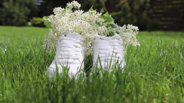 Белые кроссовки с цветами на лужайке, дует легкий ветер. Устойчивая концепция обуви. - Кадры, видео