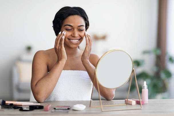 Atractiva joven mujer negra aplicando maquillaje y sonriendo - Foto, imagen