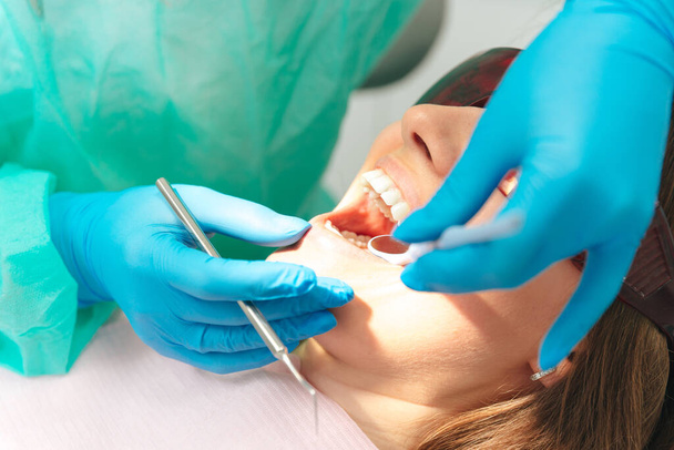 Giovane donna rimane con la bocca aperta per il dentista che esamina i denti mentre indossa vestiti e guanti usa e getta. - Foto, immagini