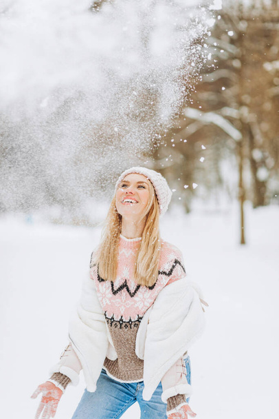 Mujer rubia feliz juega con una nieve en el día de invierno. A la chica le gusta el invierno, el día helado. Jugando con nieve en las vacaciones de invierno, una mujer lanza nieve blanca y suelta al aire. Caminar en el bosque de invierno. - Foto, imagen
