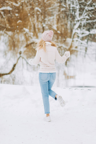 Beautiful girl in a Winter Suede Lambs Wool Jacket enjoying winter moments. Outdoors photo of blonde in a pink hat having fun on a snowy morning on a blurred nature background. - Zdjęcie, obraz