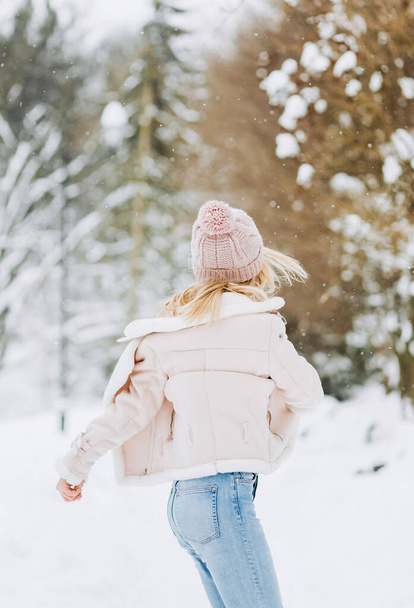 冬の瞬間を楽しむウールのセーターの美しい少女の肖像画を閉じます。ピンクの帽子をかぶった短髪の女性の屋外写真は、ぼやけた自然を背景に雪の朝を楽しんでいます. - 写真・画像