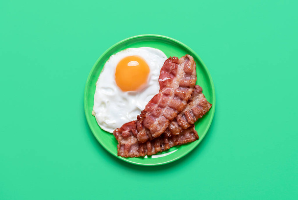 Fried egg and bacon top view, on a green table. Delicious breakfast with fried egg and bacon on a green plate. - Фото, изображение