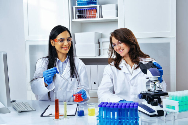 Two beautiful young female scientists working in laboratory with test tubes and microscope doing some research  - Photo, Image