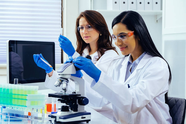 Δύο όμορφες νεαρές γυναίκες επιστήμονες που εργάζονται στο εργαστήριο με δοκιμαστικούς σωλήνες και μικροσκόπιο κάνει κάποια έρευνα  - Φωτογραφία, εικόνα