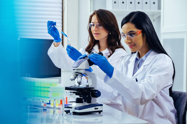 Dvě krásné mladé vědkyně pracující v laboratoři s zkumavky a mikroskop dělá nějaký výzkum  - Fotografie, Obrázek