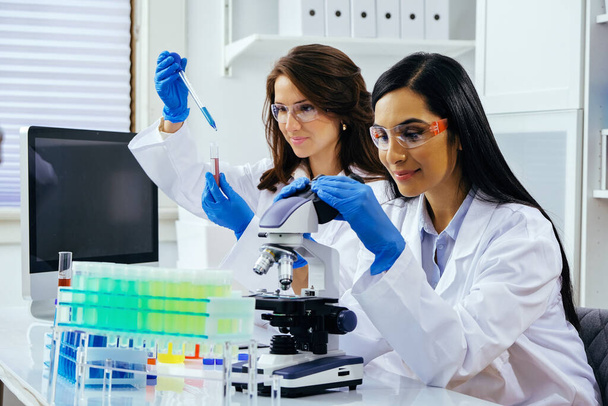 Deux belles jeunes femmes scientifiques travaillant en laboratoire avec des éprouvettes et un microscope faisant quelques recherches  - Photo, image