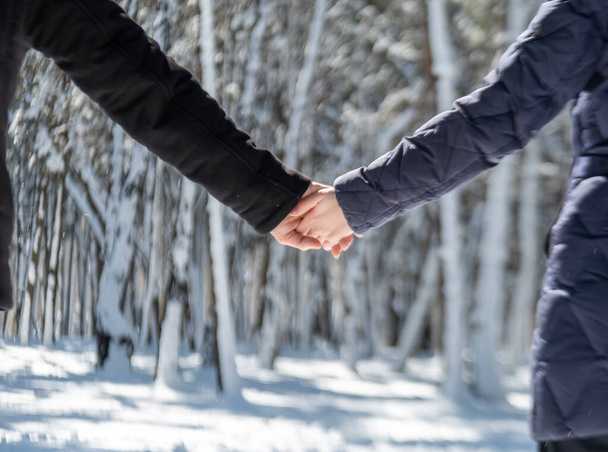 romantic young couple in a snowy winter day walking outside while holding hands in the forest. close up photo of a dating pair. Beuatiful background wallpaper - Fotó, kép