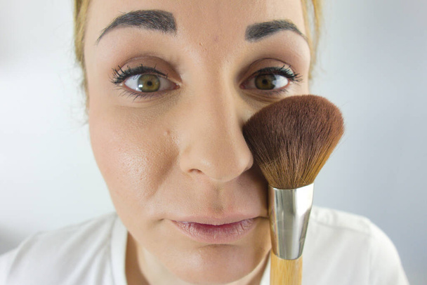 Portret van een jonge blanke vrouw met cosmetische borstel. Make-up toepassen, schoonheidsconcept - Foto, afbeelding