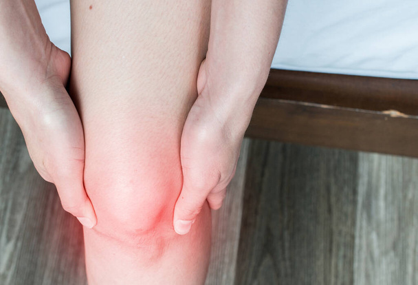 Primer plano de las manos de la mujer sosteniéndose y masajeando su rodilla, sufriendo de dolor de rodilla. El dolor de rodilla puede ser el resultado de una lesión, como un ligamento roto o un cartílago roto.. - Foto, imagen