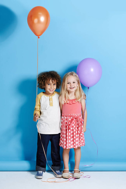 Shes my childhood sweetheart. Portrait of a cute little girl and boy holding a balloon over a blue background. - Valokuva, kuva