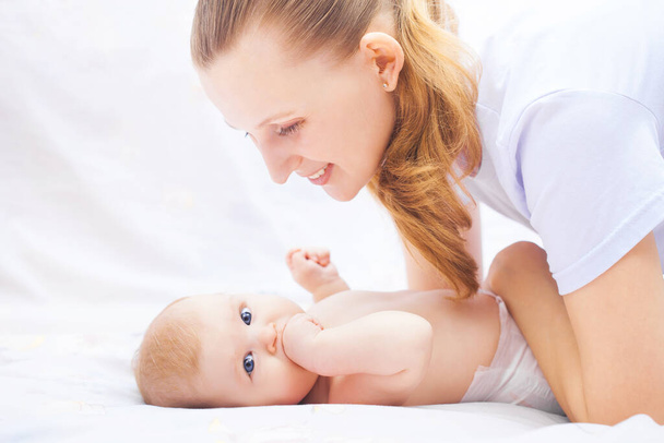 young happy mother together with her newborn baby lie cheerfully on a white bed - Foto, Bild