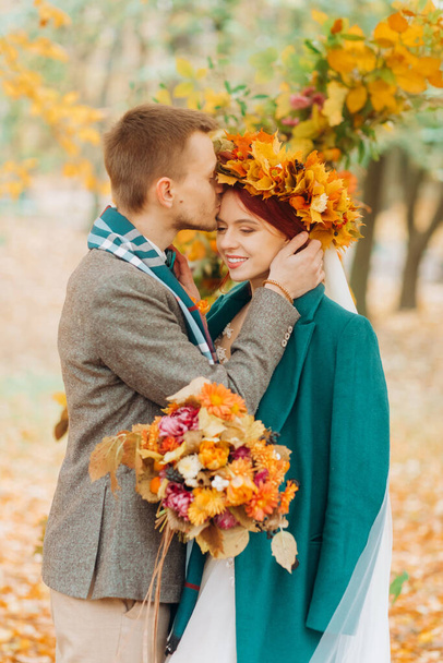 Herfst huwelijksceremonie in het park. De man kust het hoofd van zijn vrouw. - Foto, afbeelding